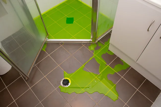 Leak detection dye test showing water tracking across a bathroom floor from a shower enclosure