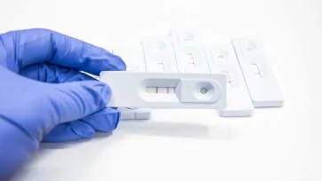 A blue-gloved hand holding a chemical testing strip