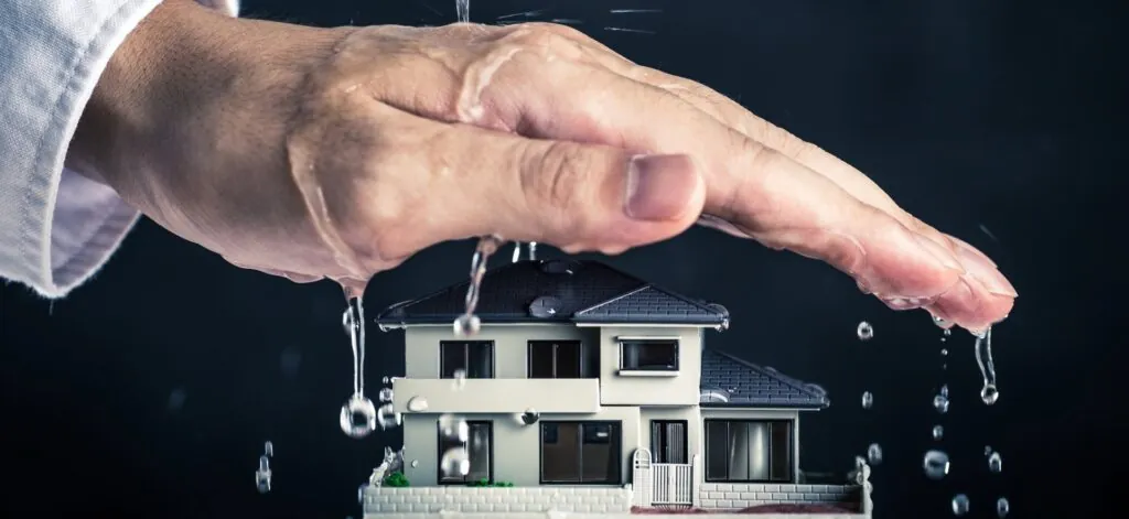 A hand protecting a miniature house from pouring water